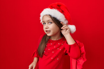 Cute hispanic girl in christmas hat over-listening to gossip, hand on ear, deafness hinted....