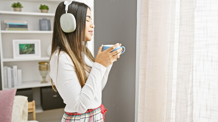 A relaxed young hispanic woman enjoys a cup of coffee at home while listening to music in her cozy bedroom.