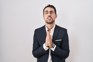 Handsome business hispanic man standing over white background begging and praying with hands...