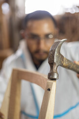 details of the construction of wooden furniture in factory interior, young man using a hammer to repair, lifestyle of artisan worker in carpentry, tool and hobbies