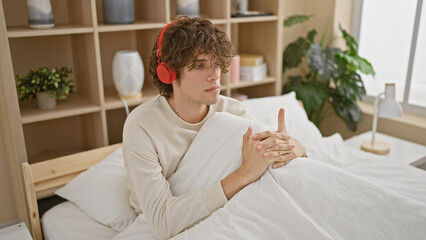 Pensive young man with headphones sitting in a bedroom, creating a relaxed, introspective atmosphere.