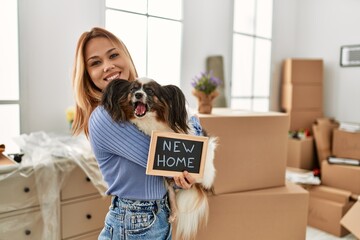 Young caucasian woman holding blackboard hugging dog at new home - obrazy, fototapety, plakaty