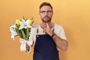 Middle age man with beard florist shop holding flowers thinking concentrated about doubt with...