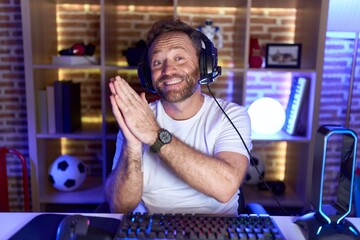 Middle age man with beard playing video games wearing headphones clapping and applauding happy and joyful, smiling proud hands together