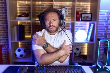 Middle age man with beard playing video games wearing headphones shaking and freezing for winter cold with sad and shock expression on face