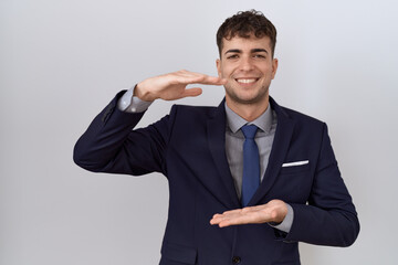Young hispanic business man wearing suit and tie gesturing with hands showing big and large size sign, measure symbol. smiling looking at the camera. measuring concept.