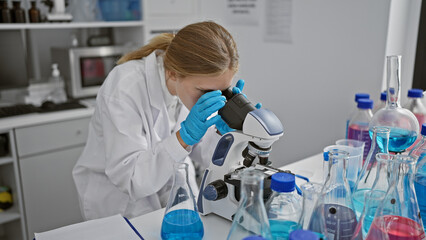 A woman scientist using a microscope in a laboratory surrounded by chemistry equipment