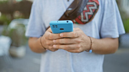 A young hispanic man with a beard uses a smartphone on a busy city street.