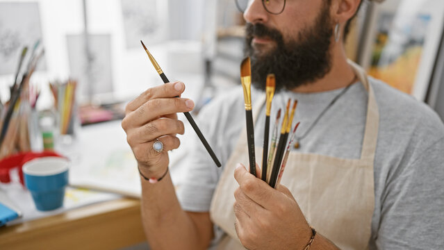Handsome hispanic man artist holding paintbrushes in a creative studio setting.