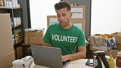 Handsome young hispanic man volunteering in community charity center, working seriously on laptop at indoor table - obrazy, fototapety, plakaty
