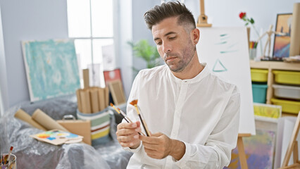 Serious-faced young hispanic man, an emerging artist, deeply engrossed in choosing the perfect...