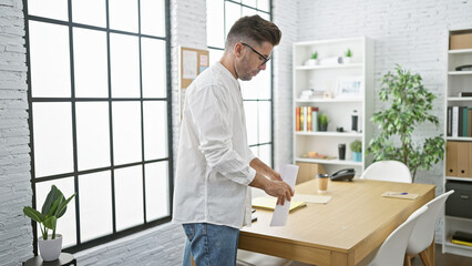 Young, serious-faced hispanic worker man holding business documents in office â€“ a picture of...