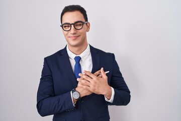 Young hispanic man wearing suit and tie smiling with hands on chest with closed eyes and grateful gesture on face. health concept.