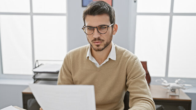 Handsome hispanic man with beard reading documents in modern office setting