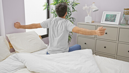 A relaxed young man stretches his arms in a bright bedroom upon waking
