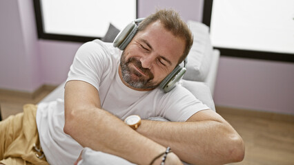 Handsome mature hispanic man enjoying music with headphones in a cozy living room setting.