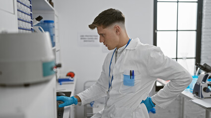 Attractive young caucasian man scientist, typing away seriously on his computer at the lab, faces a plague of backache - a grim reality of research life.