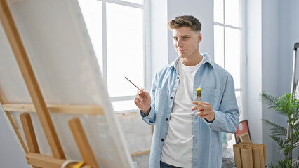 Handsome, serious caucasian artist, engrossed in his drawing, brushes and palette in hand,...