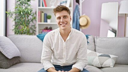 Cheerful young caucasian man enjoying a moment of relaxation, confidently sitting with a charming smile on his cozy living room sofa at home