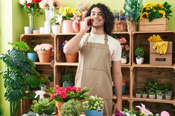 Young latin man florist smiling confident talking on smartphone at flower shop