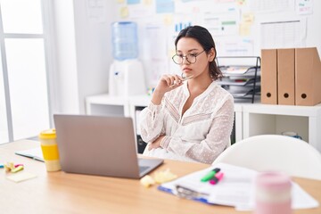 Young hispanic woman business worker using laptop with doubt expression at office