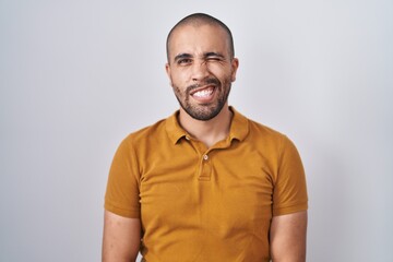 Hispanic man with beard standing over white background winking looking at the camera with sexy...