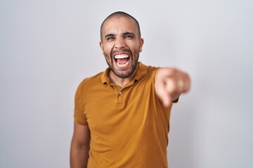 Hispanic man with beard standing over white background pointing displeased and frustrated to the...