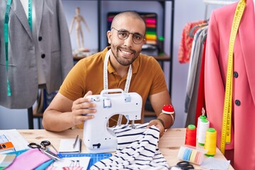 Young latin man tailor smiling confident using sewing machine at atelier