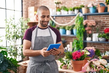 Young latin man florist smiling confident using touchpad at flower shop