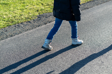 Legs of a child in jeans and sneakers on the road.