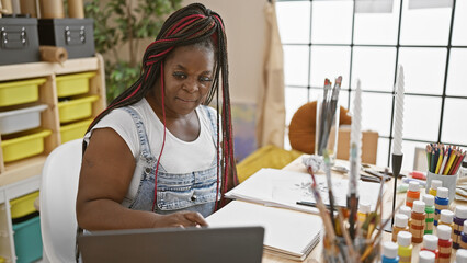 Beautiful african american woman artist, relaxed with braids, painting her life on notebook,...