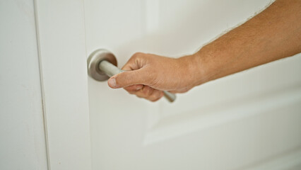 Obraz premium Closeup of a male hand gripping a modern doorknob to enter or exit a white interior room.