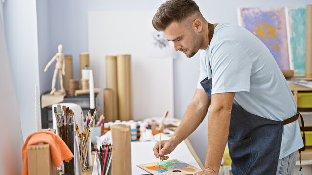 Handsome hispanic man painting with a brush in an art studio.