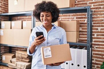 African american woman ecommerce business worker using smartphone holding package at office