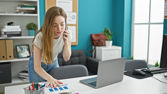 Young blonde woman business worker talking on smartphone reading document at the office
