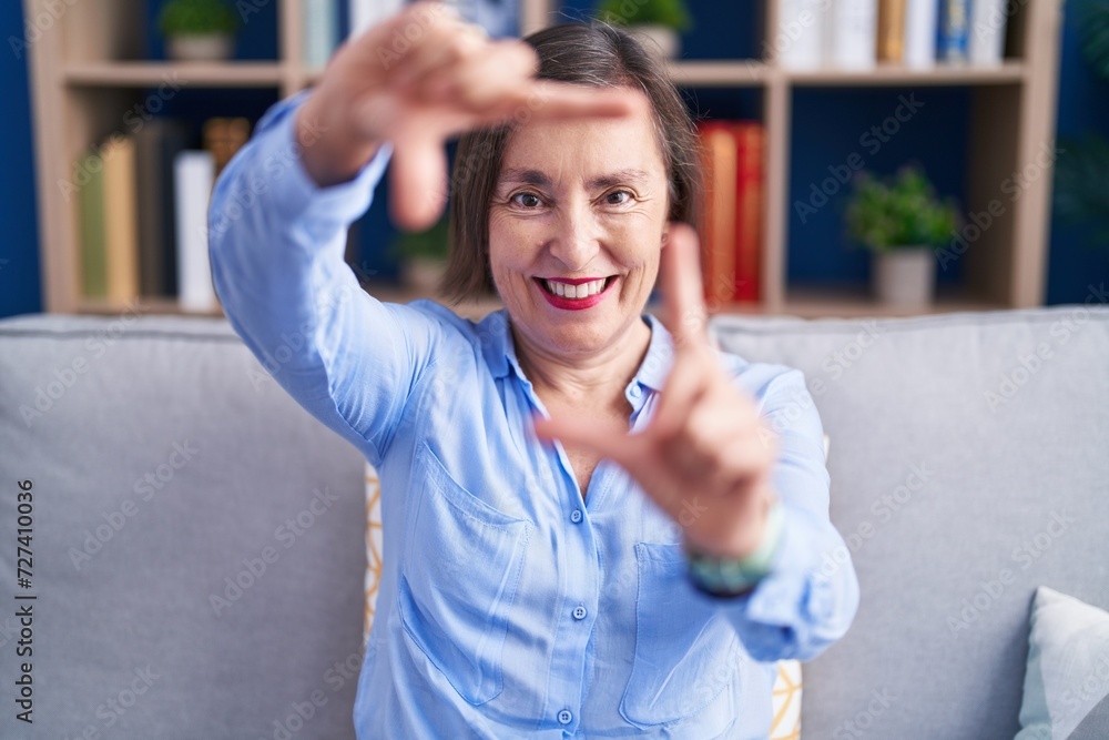 Canvas Prints Middle age hispanic woman sitting on the sofa at home smiling making frame with hands and fingers with happy face. creativity and photography concept.