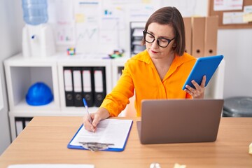 Middle age woman business worker using touchpad writing on document at office