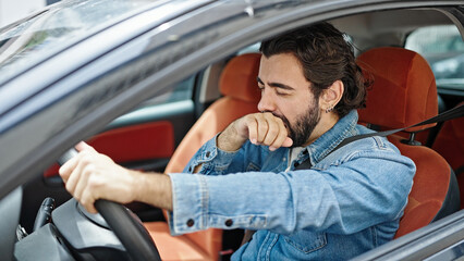 Young hispanic man tired driving car yawning at street