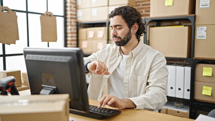 Young hispanic man ecommerce business worker using computer looking watch at office