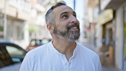 A bearded senior hispanic man smiling outdoors on a sunny city street