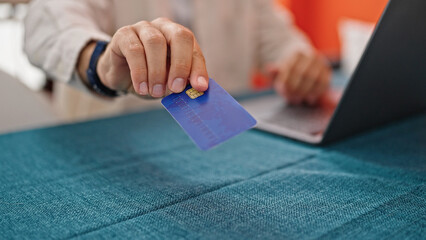 Young hispanic man using laptop and credit card sitting on table at dinning room