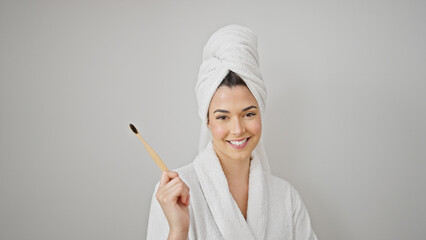Young beautiful hispanic woman wearing bathrobe holding toothbrush over isolated white background