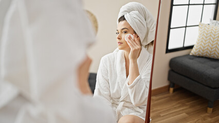 Young beautiful hispanic woman wearing bathrobe cleaning face with cotton pads at bedroom