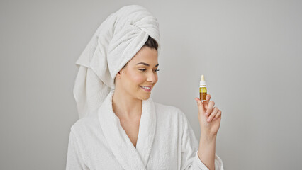 Young beautiful hispanic woman wearing bathrobe holding serum bottle over isolated white background