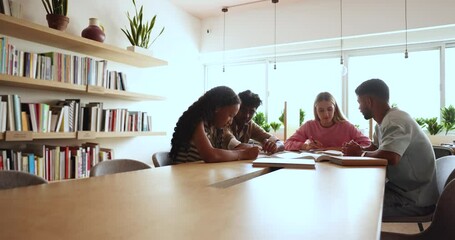 Four diverse schoolmates talking sit at desk in college library, share thoughts and opinions, working on joint project, prepare exercise, studying together. Education, knowledge and skills development