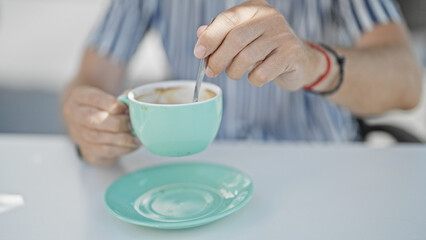 Close-up of a man stirring coffee in a turquoise cup at a modern cafe terrace.