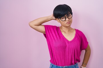Young asian woman with short hair standing over pink background confuse and wondering about...