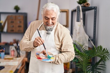 Middle age grey-haired man artist smiling confident holding paintbrush and palette at art studio
