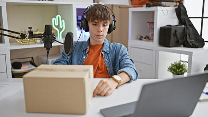 A teenage boy podcasts at a home studio setup with a microphone, headphones, laptop, and a package,...
