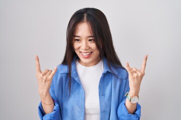 Young chinese woman standing over white background shouting with crazy expression doing rock symbol...